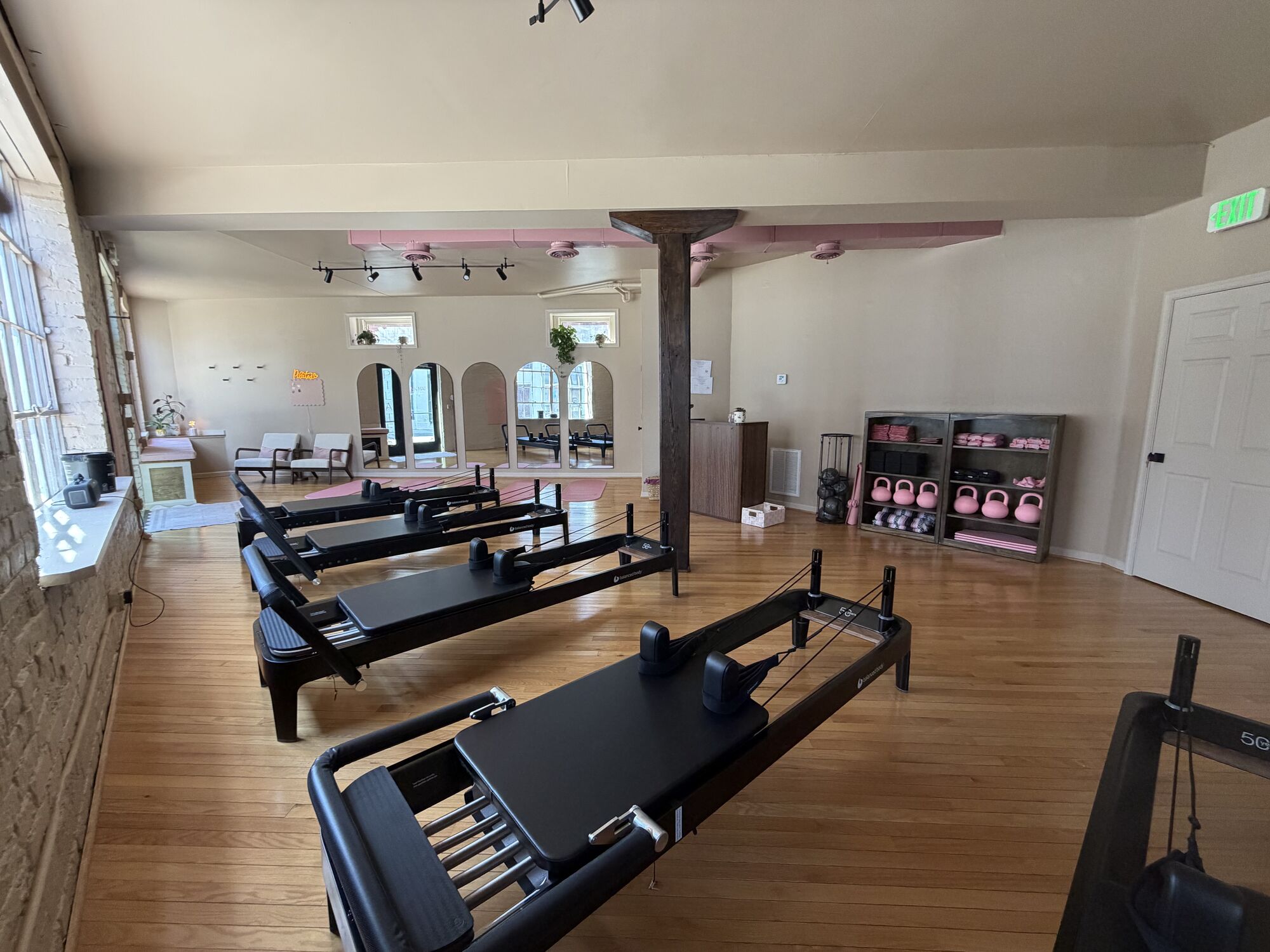 Six reformers lined up across the warm wood floor of The Pink Mat studio