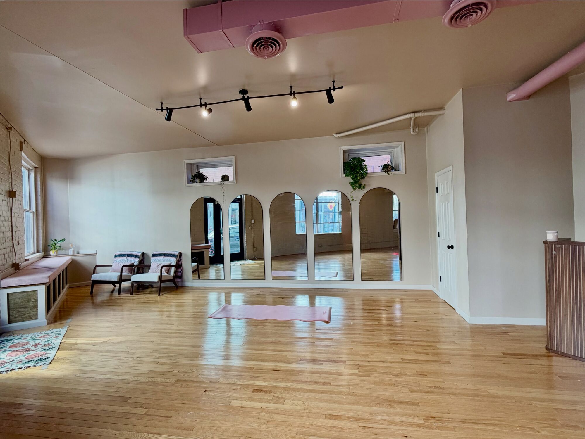 The bright front room of The Pink Mat with honey wood floors, arched mirrors and a single pink mat laid out